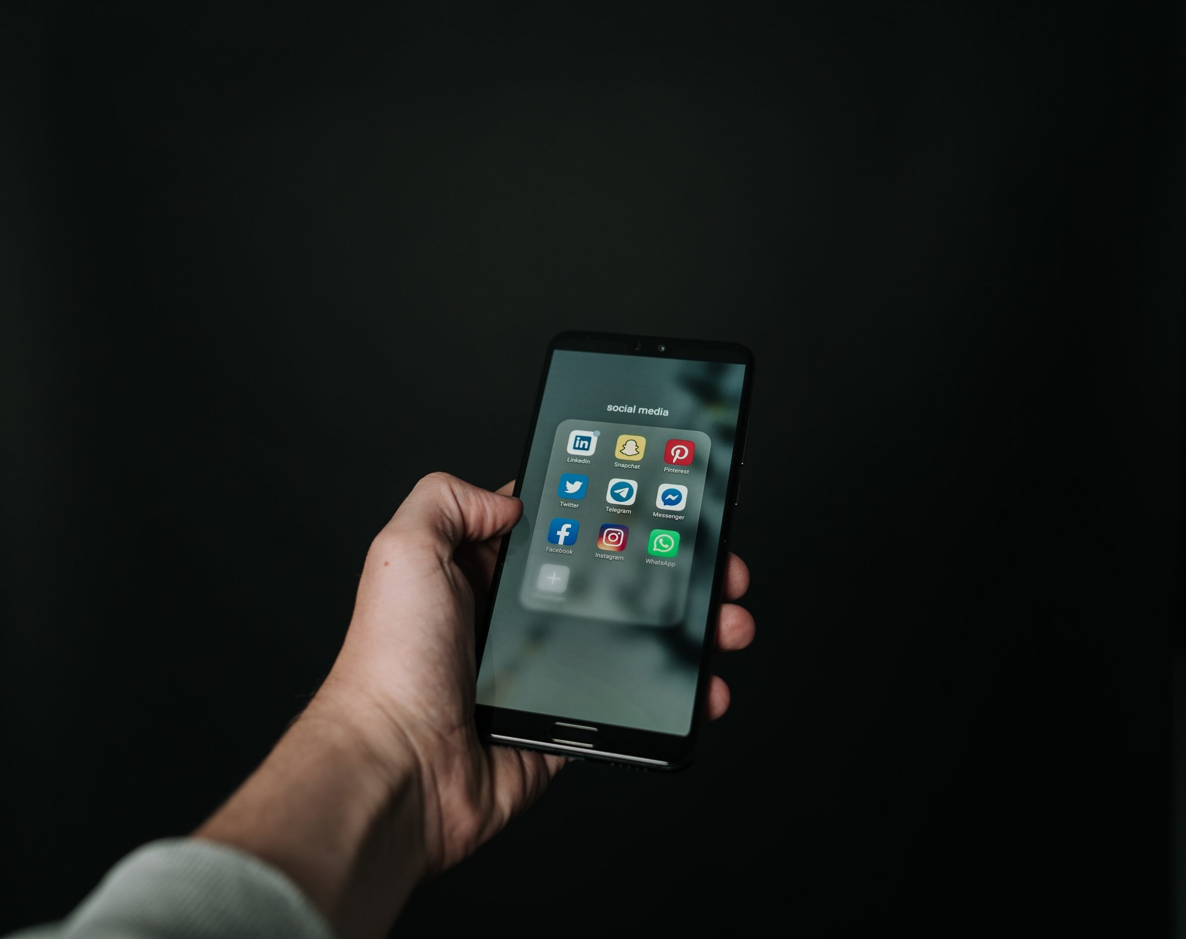 Hand holding a phone showing various social media apps